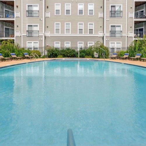 Sparkling swimming pool The pool area at Jefferson at Dedham Station apartments in Dedham, MA, featuring lounge chairs and umbrellas.
